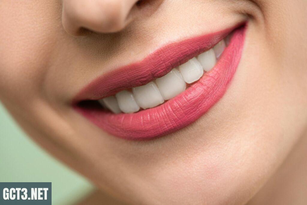 Vivid close-up image of a woman's smile showcasing red lipstick and white teeth on a light background.